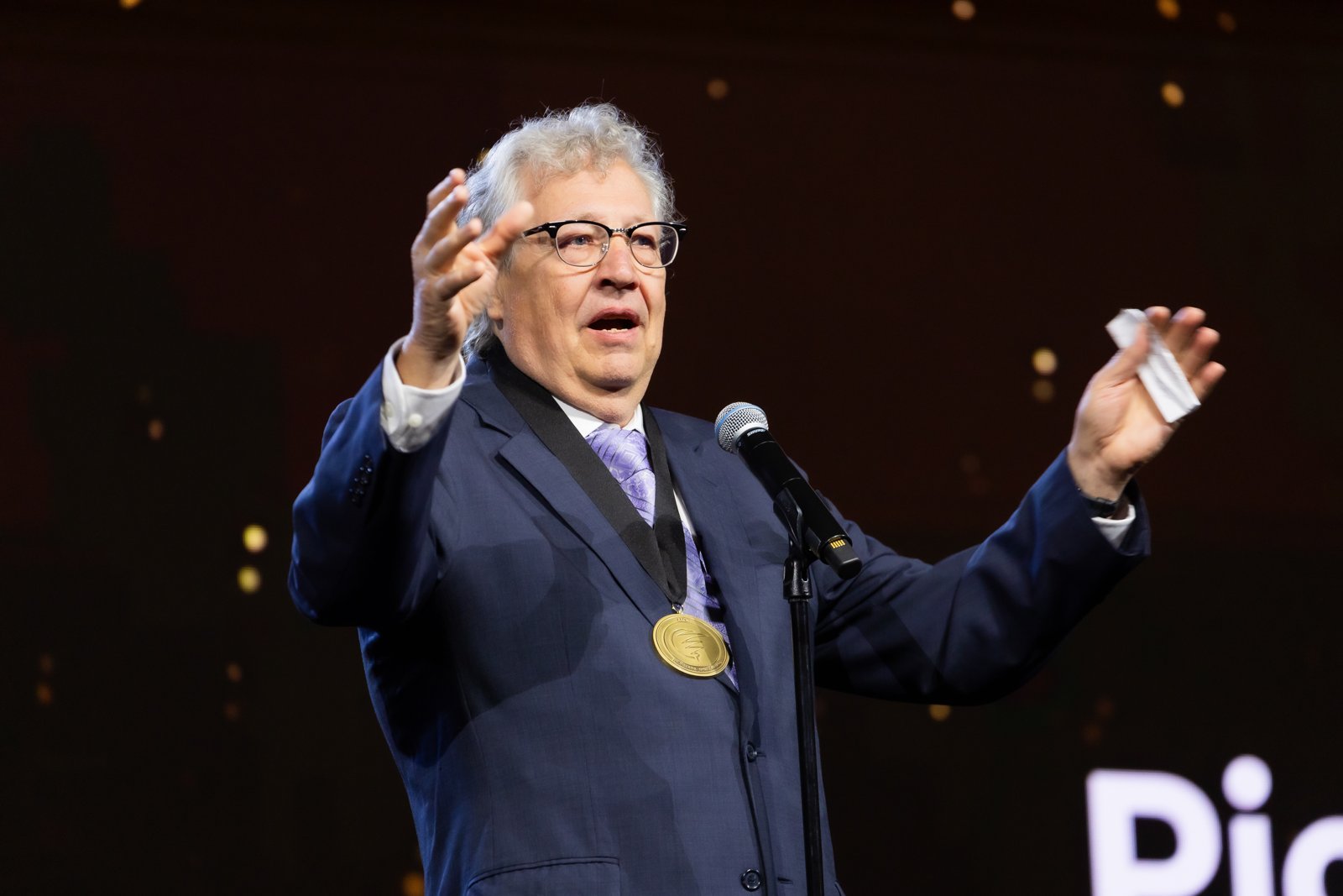 Dr. Mike Ackerman wearing the AACN Pioneering Spirit Award medal while speaking on stage at NTI